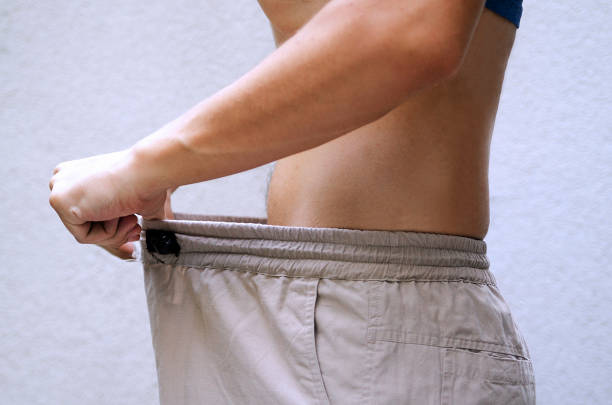 Young man showing how much he got his weight lost by pulling his pants.Guy checking size his genital Man after diet comparing his waist size of trousers.Slim fit male body or genital issue. condom photos stock pictures, royalty-free photos & images
