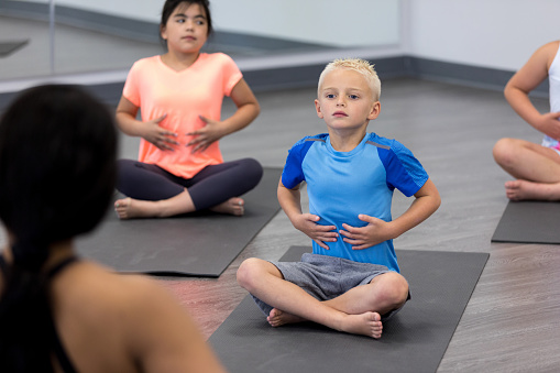 A group of young children watches unrecognizable yoga teacher to learn how to breathe properly.