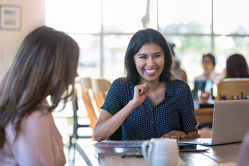 During the meeting at the coffee shop, female coworkers share a laugh.