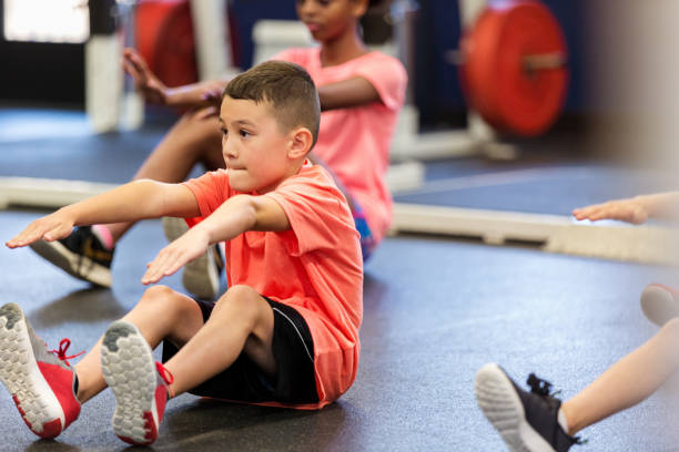 Little boy exercises during PE class Elementary schoolboy concentrates while performing a sit up during fitness class or PE class. touching toes stock pictures, royalty-free photos & images