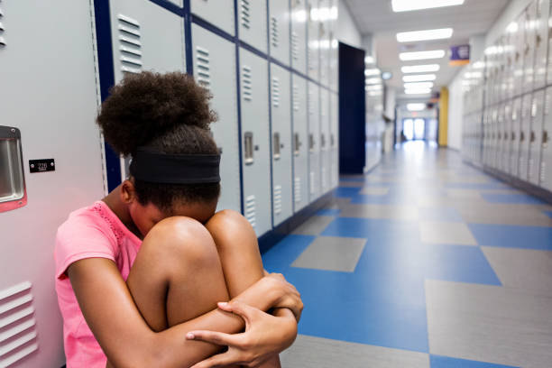 Lonely preteen student in locker room Sad preteen girl hides her head in her knees while sitting in a school hallway or locker room. school exclusion stock pictures, royalty-free photos & images
