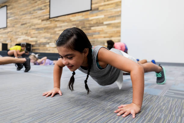 petite fille faisant des pompes dans la classe de gymnastique - éducation physique photos et images de collection