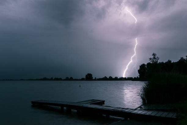 scenic night view of a pier at the shore of a lake while lightning strikes in the background - ocean scenic flash imagens e fotografias de stock