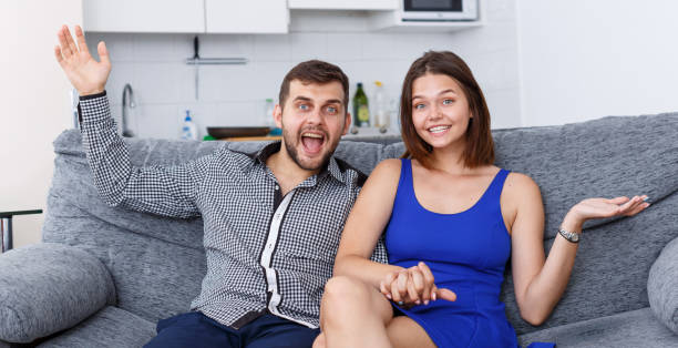 istock Smiling young couple sitting on sofa at home watching TV 1172577343