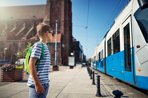 Little boy waiting for a tram on a tram stop. The boy is looking at the approaching train and is getting ready to get on it on his way to school.
Nikon D850