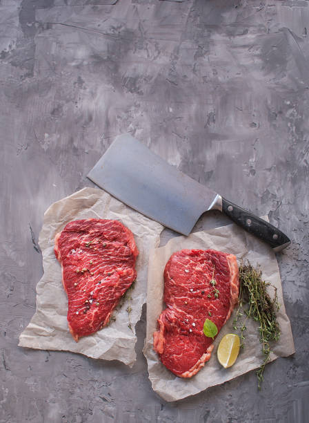 Fresh raw beef steak Mignon, with salt, pepper, thyme, lemon on a black textured concrete background. The view from the top. Copy space