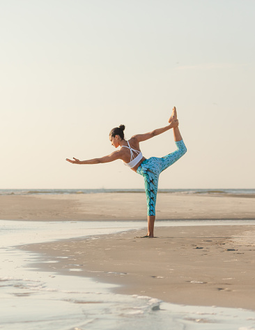 A young African-American woman does Dancer Pose at the beach.