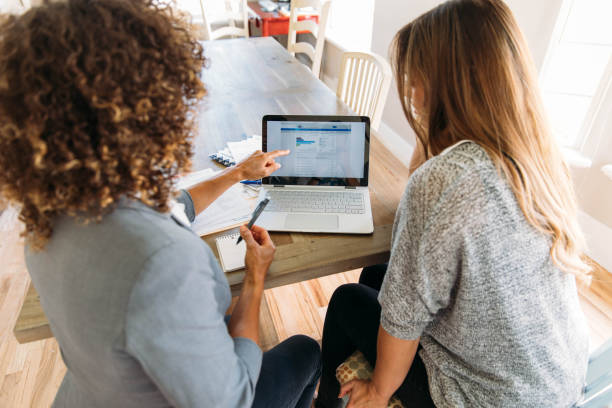 Personal Financial Help with Financial Advisor A female financial advisor sits with a woman at her dining room table with laptop and financial reports helping her monthly budget and investments. She is showing her client how to read a financial report as she works on her computer to do monthly finances, pay taxes and save money for the future. customized data stock pictures, royalty-free photos & images