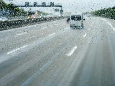 Elevated view over the front driving white van car through the covered with raindrops windshield of bus coach or truck - motion on German autobahn