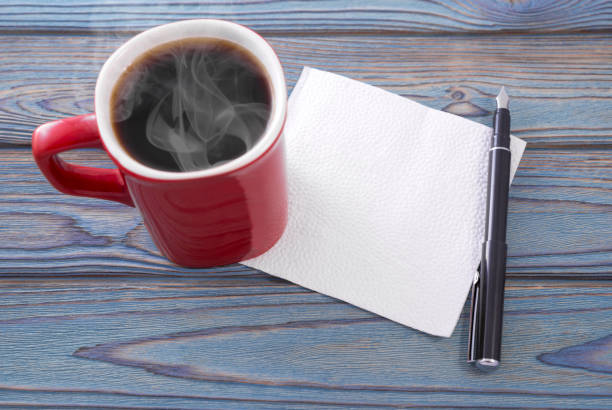 Red cup of hot coffee with a napkin on the table. A pen. Place for text