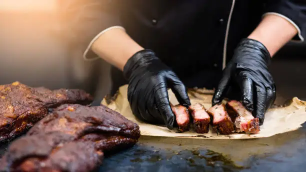 Grill restaurant kitchen. Cropped shot of chef in black cooking gloves serving smoked pork ribs.