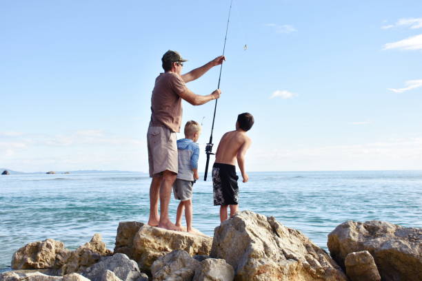 Children and Father Fishing on Coastal Rocks A Father and his Children on a Fishing Trip off Coastal Rocks in summer. fishing rod photos stock pictures, royalty-free photos & images