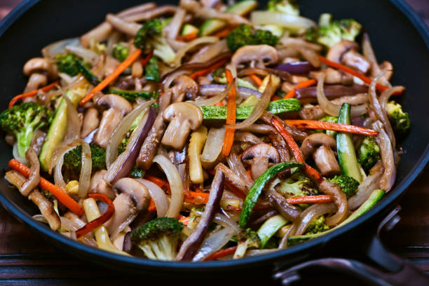 Sauteed Chopped Vegetables in Juliana: Zucchini, Onions, Eggplant, Carrots, Mushrooms and Broccoli inside an professional anodized nonstick aluminum skillet over a vintage wooden surface.
