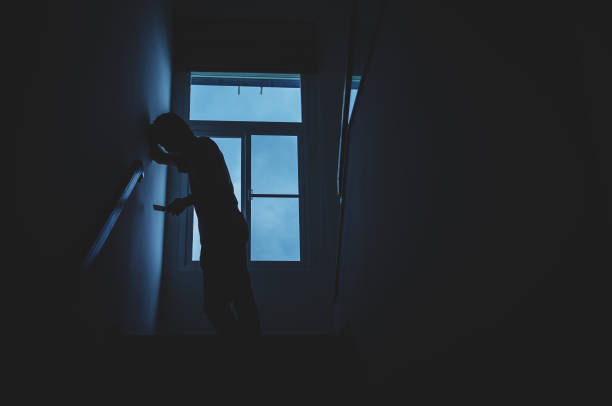 istock Alone man silhouette standing using phone at the window closed in darkhome. Man stands at window alone, Depression and anxiety disorder concept. 1172633046
