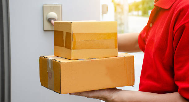 istock Young delivery man in red uniform standing with parcel post box press ring bell in front of the house to delivery of the good, The delivery service concept, Deliver packages to recipients quickly. 1172633057