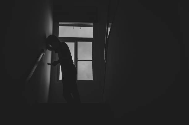 istock Alone man silhouette standing using phone at the window closed in darkhome. Man stands at window alone, Depression and anxiety disorder concept. 1172633067