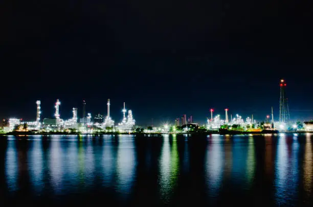 Night scene of oil refinery plant of Petrochemistry industry in twilight time and reflection in near river, gas and oil production processing in Bangkok, Thailand.