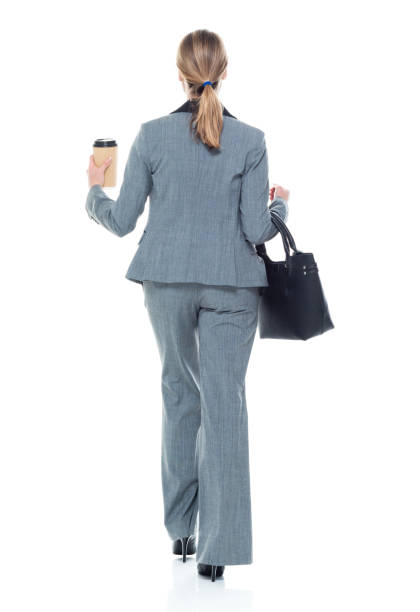 rear view / full length of 20-29 years old adult beautiful caucasian female / young women businesswoman / business person walking in front of white background wearing a suit and holding briefcase / bag / coffee cup - one young woman only only young women one woman only 20 25 years imagens e fotografias de stock