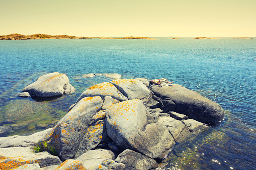 Holiday summer in Sweden Island with woman on holiday lay on the rock relaxing taking sunbath with blue sea and colour sky as background