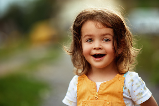 Little girl with brown hair outdoors, looking at the camera happily