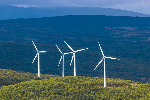 Four white wind turbines in sunshine on Arctic mountain range in Swedish Lapland with dark background