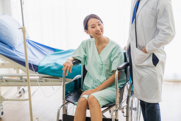 professionelle ärzte und frauen falten gebrochenen arm mit bandage der hand, während patient sitzen auf rollstuhl im krankenhaus - singapore mrt stock-fotos und bilder