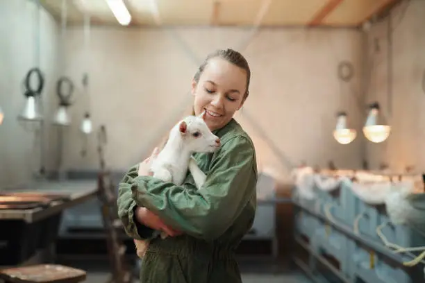 Shot of a young woman holding an adorable baby goat at a dairy farm