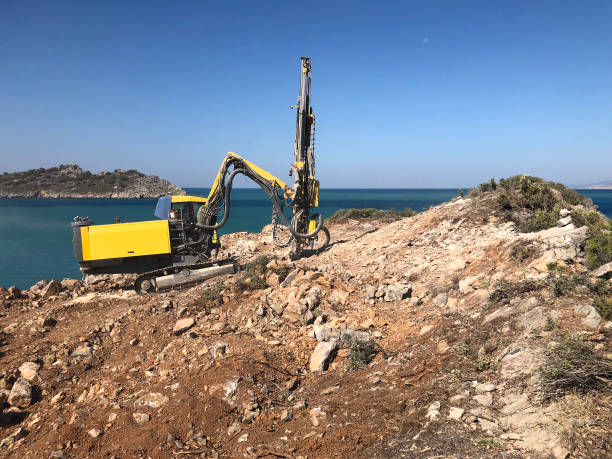 yellow machinery is drilling holes on the top of rocky sea cliff during blasthole drilling operations - drill borehole mining rock imagens e fotografias de stock