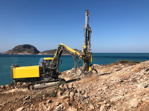 yellow machinery is drilling holes on the top of rocky sea cliff during blasthole drilling operations - drill borehole mining rock imagens e fotografias de stock