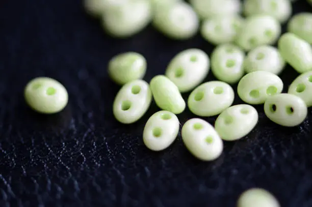 Twin beads light green color scattered on a dark surface close up
