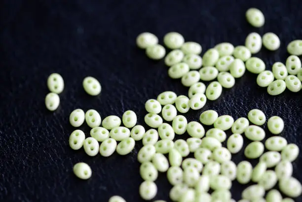 Twin beads light green color scattered on a dark surface close up
