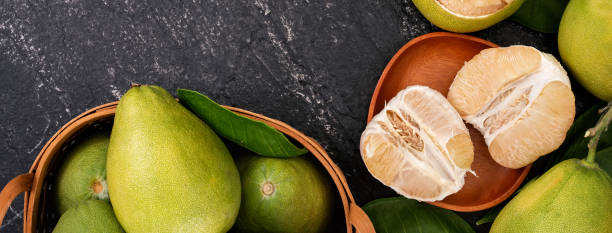 pomelo fresco, pompelmo in cesto di bambù con foglia verde su sfondo ardesia nero scuro. frutta di stagione per la festa di metà autunno. - fruit table bamboo black foto e immagini stock