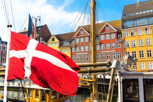 コペンハーゲンの象徴的な眺め。コペンハーゲンの中心部にある有名な古いニューハウン港は、前景にデンマークの旗を持つ夏の晴れた日にデンマークの中央に。 - denmark ストックフォトと画像