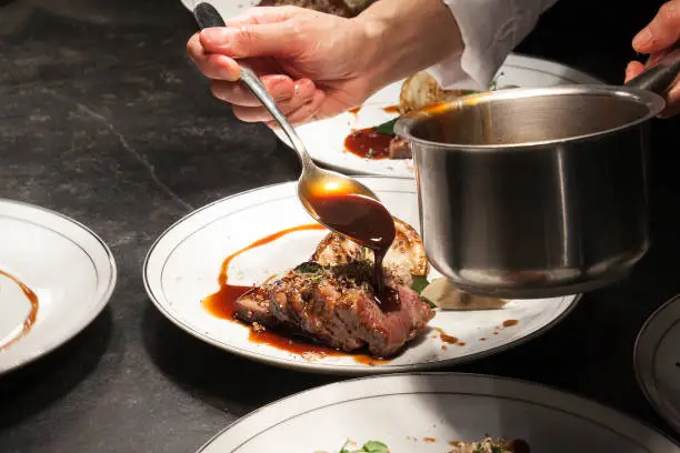 Blurry background of the chef is pouring the sauce on beef is main dish.