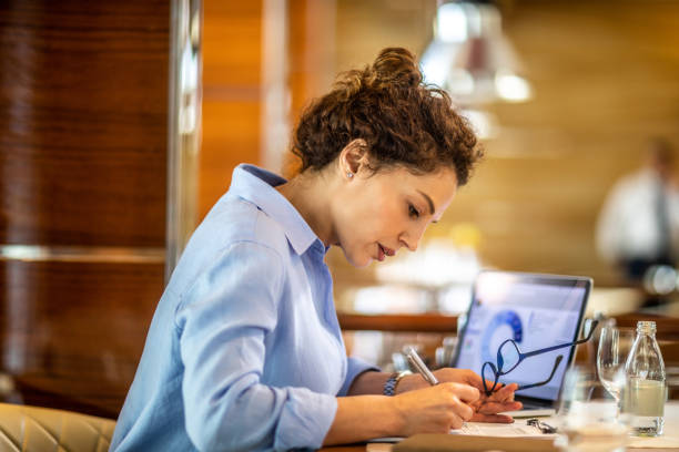 Female entrepreneur writing something down while sitting in an exclusive restaurant stock photo