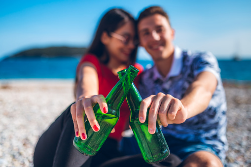 Young caucasian heterosexual couple enjoying in sunny day on beach with beer.