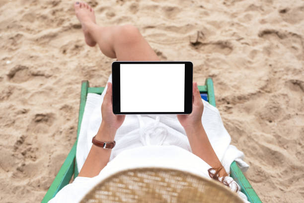 istock a woman holding and using a black tablet pc with blank desktop screen while laying down on a beach chair 1172677324