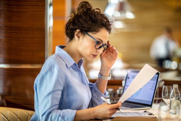 female small business owner reading a paper document while sitting in a restaurant - despair finance report business imagens e fotografias de stock