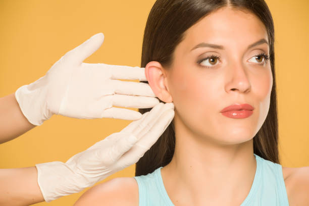 Doctor's hands touching the nose of a young woman on yellow background stock photo