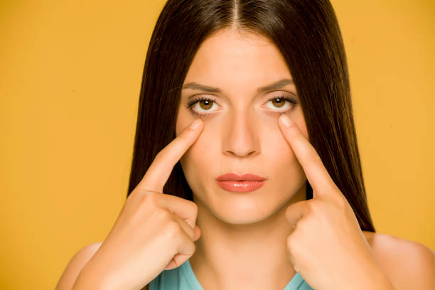 istock Young woman touching her  low eyelids on yellow background 1172681819
