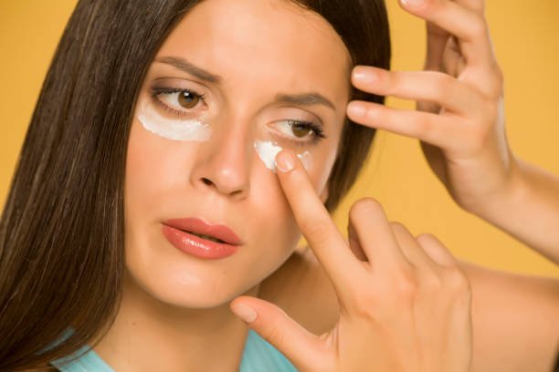 istock Young woman applying a creme on her  low eyelids on yellow background 1172681861