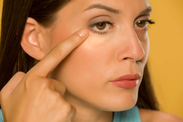 istock Young woman touching her low eyelids on yellow background 1172681896