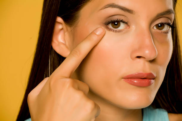 istock Young woman applying concealer on her  low eyelids on yellow background 1172681911
