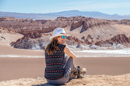 Young blond caucasian woman alone sitting and admiring untouched nature of Moon Valley in Atacama desert, Chile. Outstanding landscape background with copy space
