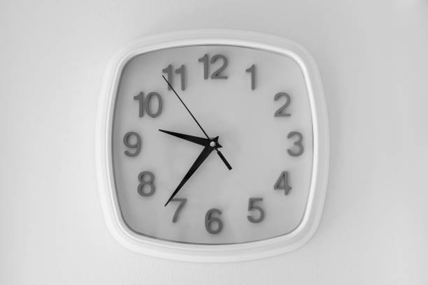 istock White clock hanging at the wall. black and white background 1172685350