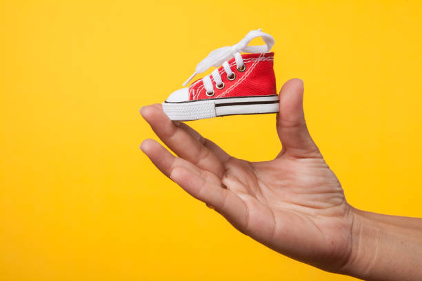 istock hand holds baby shoes on a string on a yellow background 1172685613