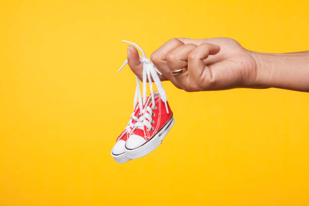 istock hand holds baby shoes on a string on a yellow background 1172685662