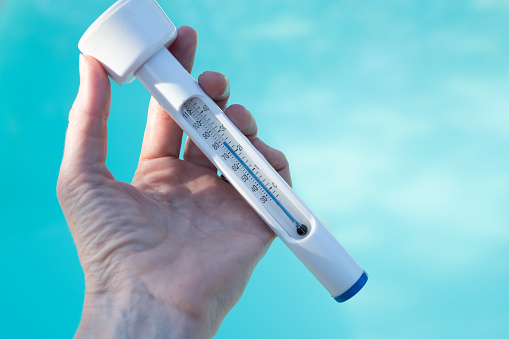 Checking the temperature of the swimming pool water with a thermometer