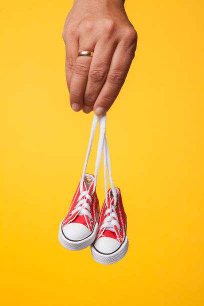 istock hand holds baby shoes on a string on a yellow background 1172688540