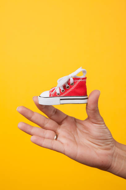istock hand holds baby shoes on a string on a yellow background 1172688559